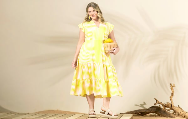 Model is wearing a yellow plus size midi dress and holding a basket of lemons.