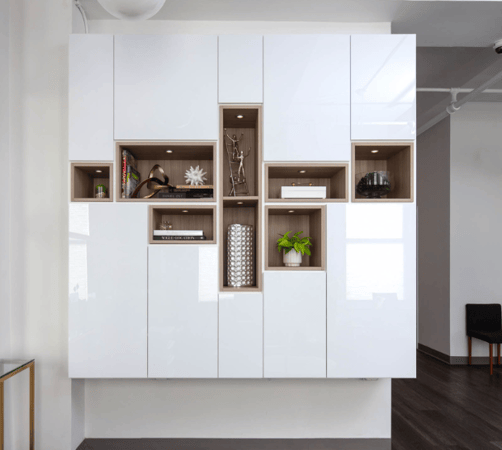modern white high gloss shiny wall unit in drs office waiting room with different sizing natural wood cubbies in the middle for display collectibles with puck lighting Westchester NY