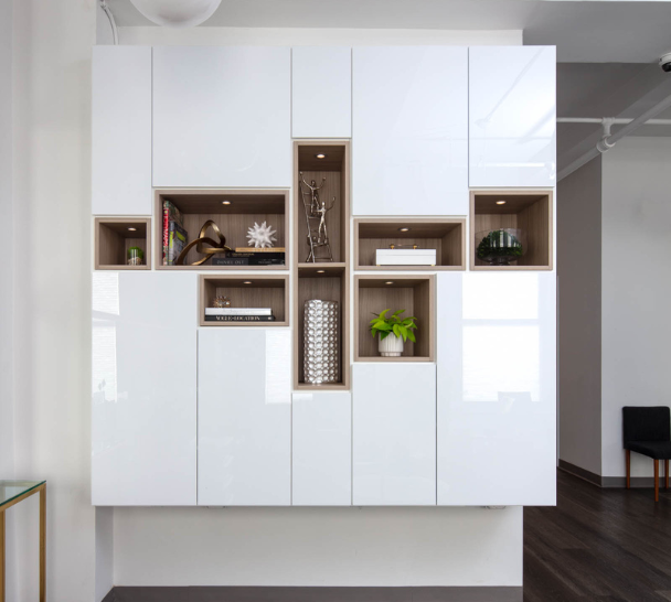 modern white high gloss shiny wall unit in drs office waiting room with different sizing natural wood cubbies in the middle for display collectibles with puck lighting Westchester NY