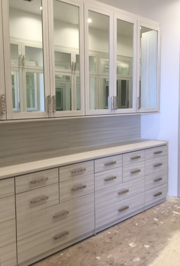 Floor to ceiling wardrobe system in a light finish with drawer stacks and mirror glass doors on upper cabinets.