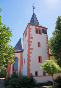 Außenansicht der weißen Kirche mit roten Akzenten. Die Kirche ist umgeben von Bäumen.