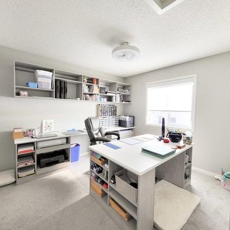 Light grey craft room with a center island work station, open shelving, drawers.