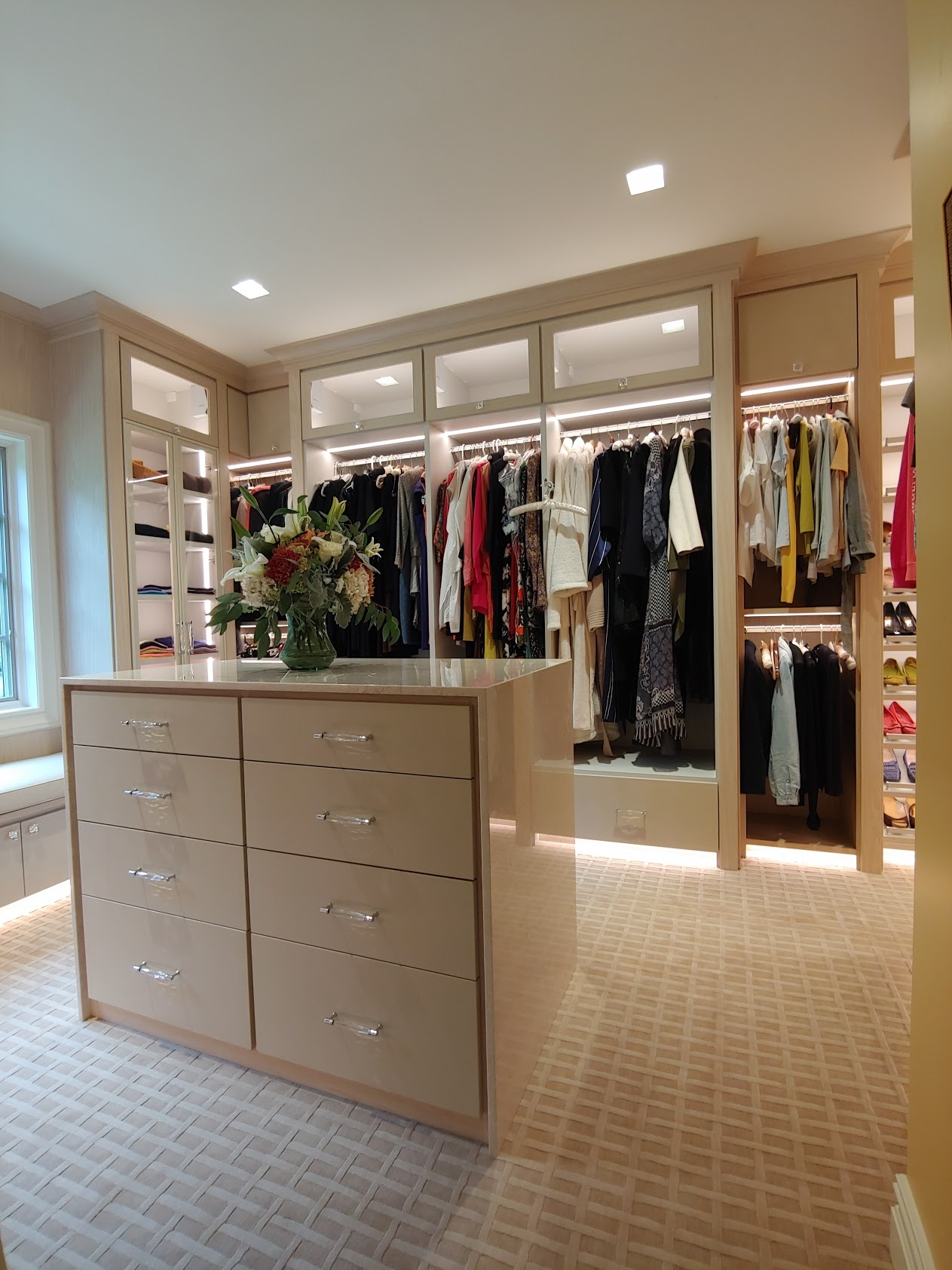 Walk-in closet with island in light wood color with lighting