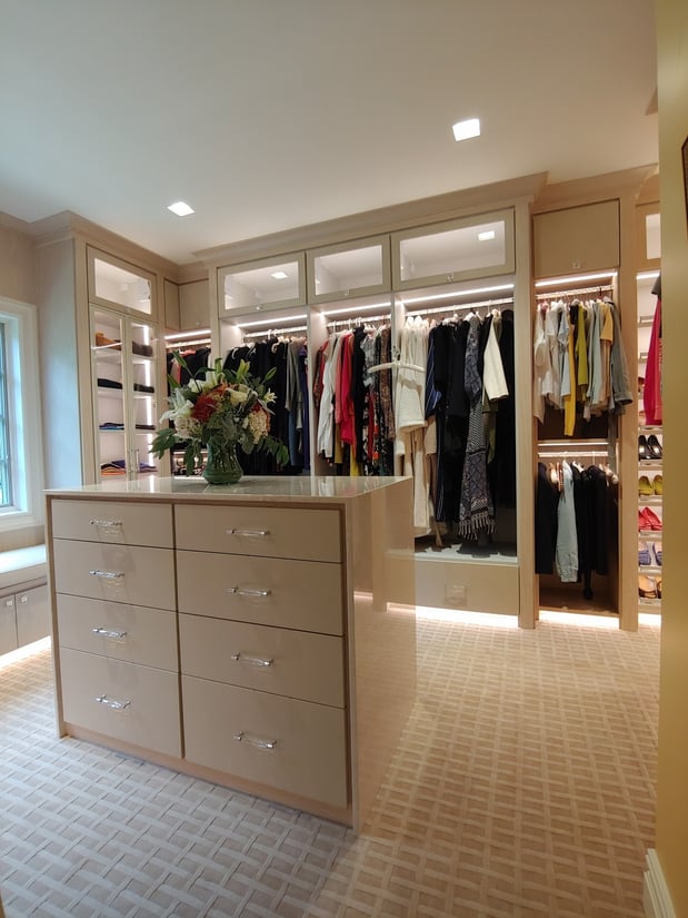 Walk-in closet with island in light wood color with lighting