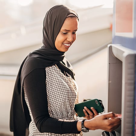 A woman holding a smartphone and using an ATM