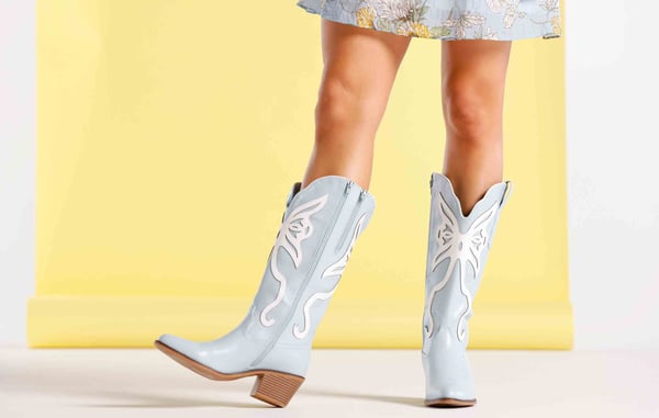 Woman is wearing light blue tall cowboy boots from Versona with her mini dress.