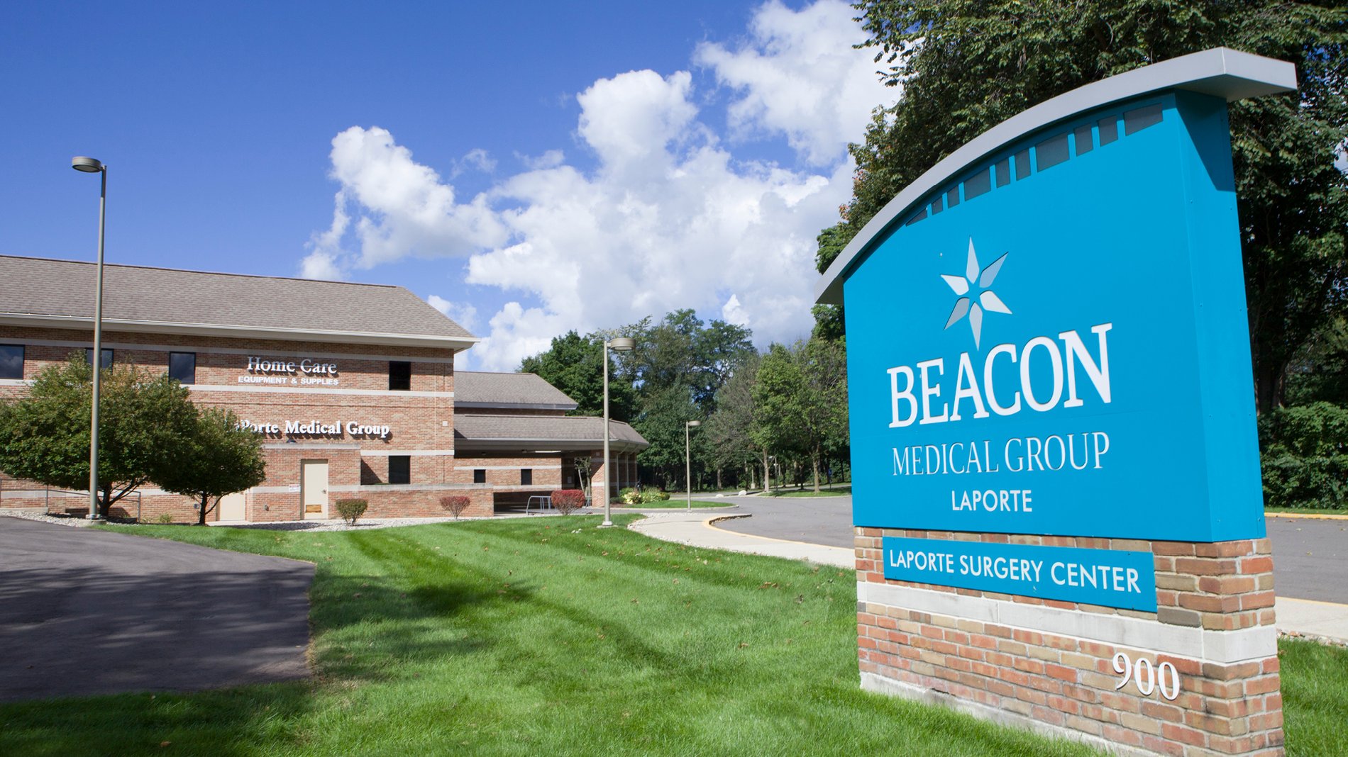 A teal sign stands in grass in front of the Beacon Medical Group LaPorte building.