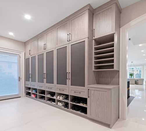 Custom mudroom lockers with tall cabinets, shoe cubbies, drawers, and open shelving in a bright, modern entryway.