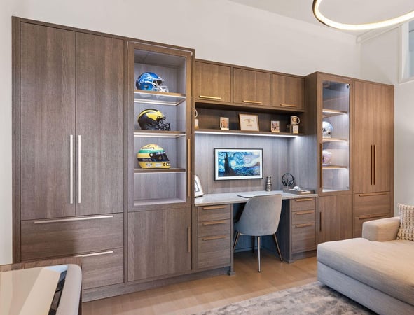 Home office with brown wood grain boards, gold pull handles, glass doors, and integrated lighting