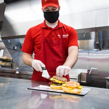 A Five Guys crew member constructs a cheeseburger
