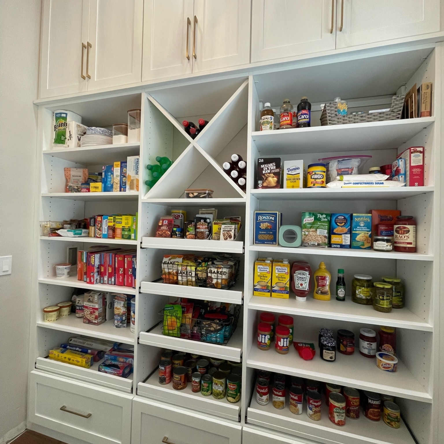Custom walk-in pantry with white built-in shelving, organized food storage, wine cubbies, drawers, and upper cabinetry.