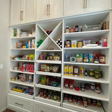 Custom walk-in pantry with white built-in shelving, organized food storage, wine cubbies, drawers, and upper cabinetry.
