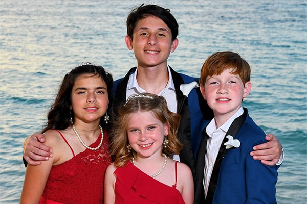 Four children in formal attire standing for a group photo in front of the ocean.