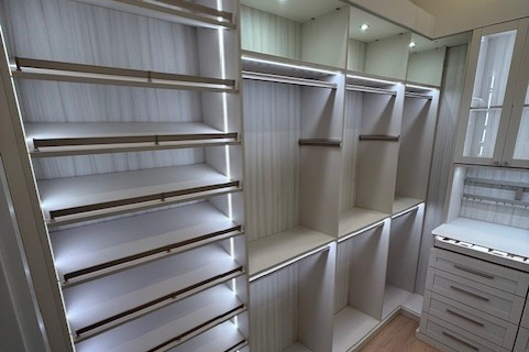 Custom primary closet in Linen with Tuscan Moon backing, featuring shaker drawers, Chroma Whiteout countertop, Paxton handles in matte nickel, Everstyle accessory drawers, TAG Maddox accents, slanted shoe shelving, and a tilt-out hamper.