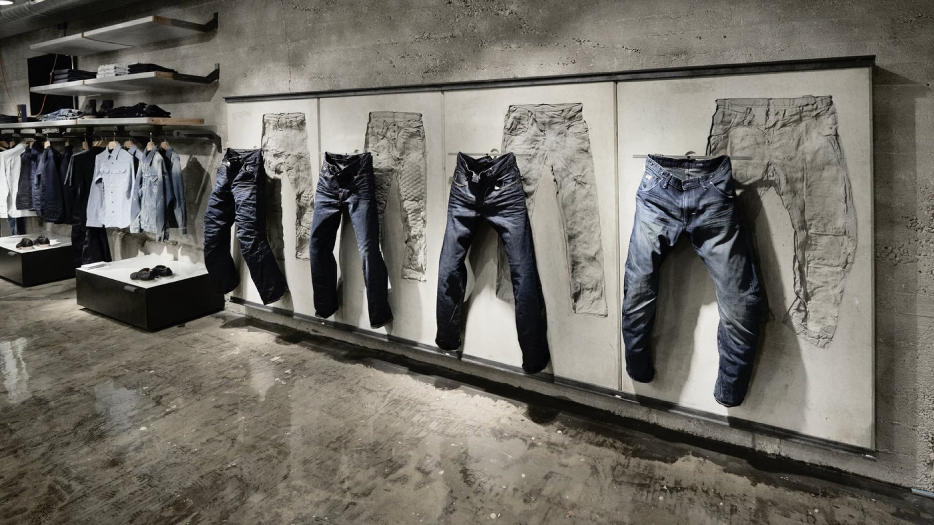 Jeans hang against an industrial cement wall alongside button down blue dress shirts.