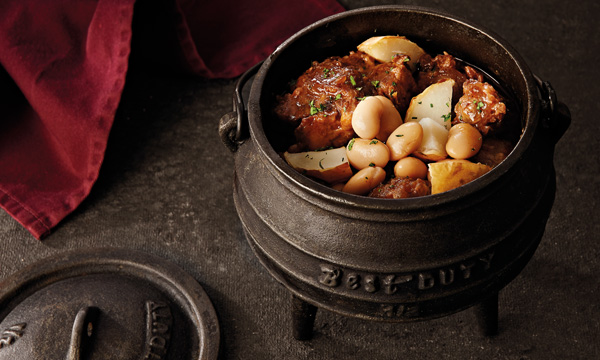 Braised oxtail in a potjie pot on a wooden table.