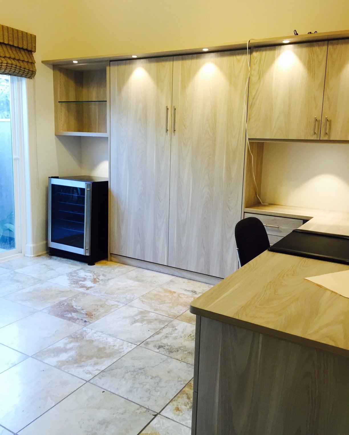 An office space doubles as a guest room with a wall bed and storage by California Closets Hawaii.