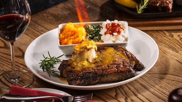 600g rib-eye steak topped with compound butter and roasted bone marrow being melted by a blowtorch with steakhouse sides and a glass of red wine from the Turn ‘n Tender menu.