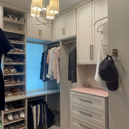 Linen-finish bedroom closet with gold hardware, shaker doors, and a petal pink back-painted glass countertop.