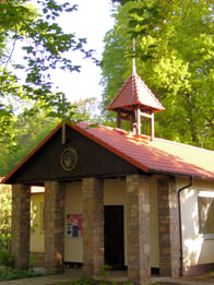 Die Waldkapelle dargestellt in der Außenansicht von vorne. Im Hintergrund sind einige grüne Bäume zu erkennen.