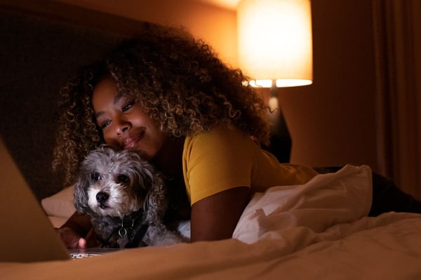 Women in bed using laptop while also hugging her dog.