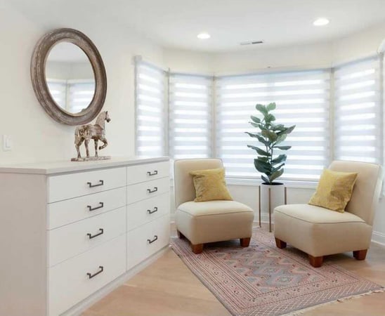 dresser with round mirror and two chairs with table and plant in between