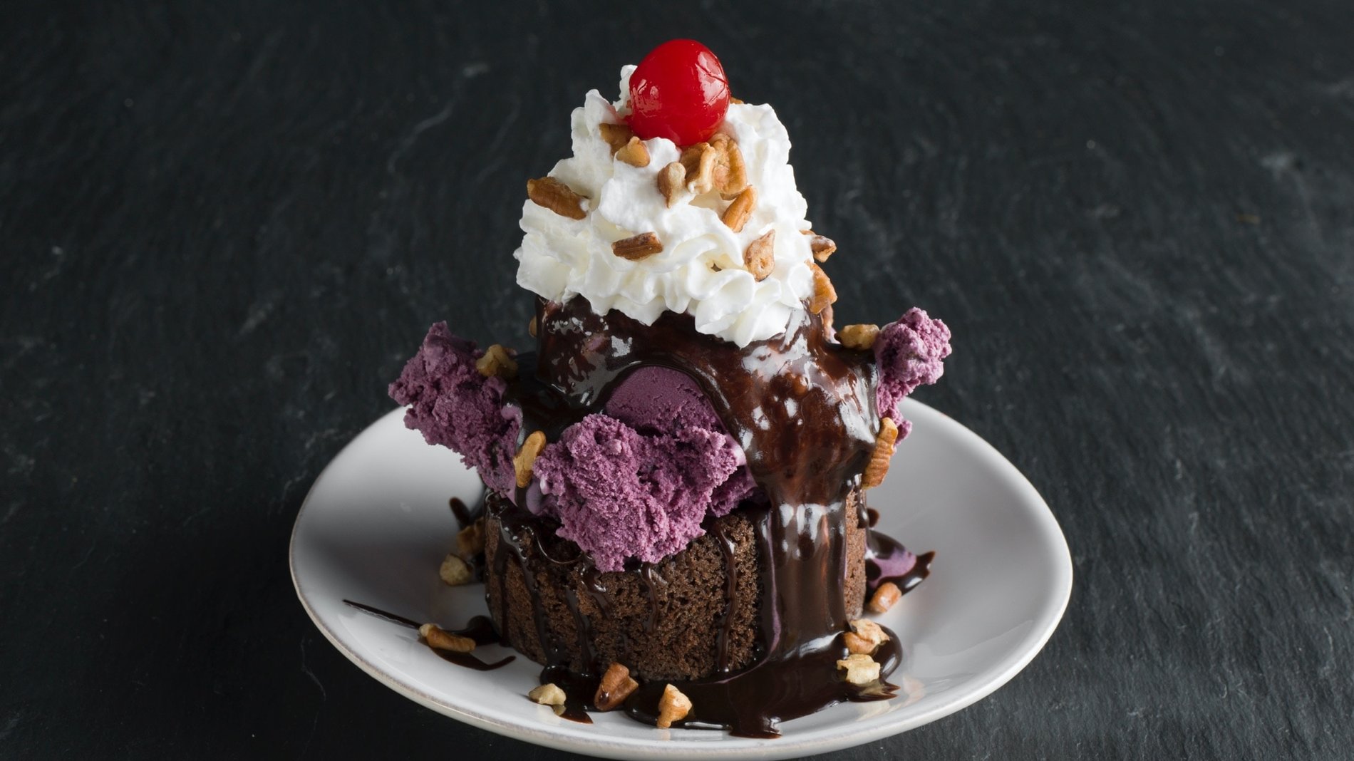 A Graeter's 1870 Tower Sundae, A fresh chocolate bundt cake filled with hot fudge, a scoop of black raspberry chocolate chip ice cream, drizzle with hot fudge, topped with fresh whipped cream, pecans and a cherry.