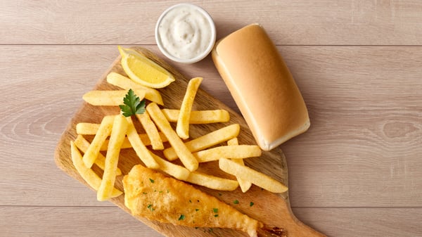 Baby hake with chips on a wooden board next to a mini loaf and sauce.