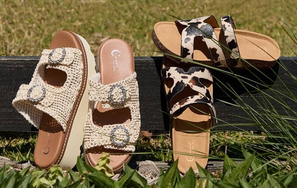 Two pairs of sandals are displayed in the grass.
