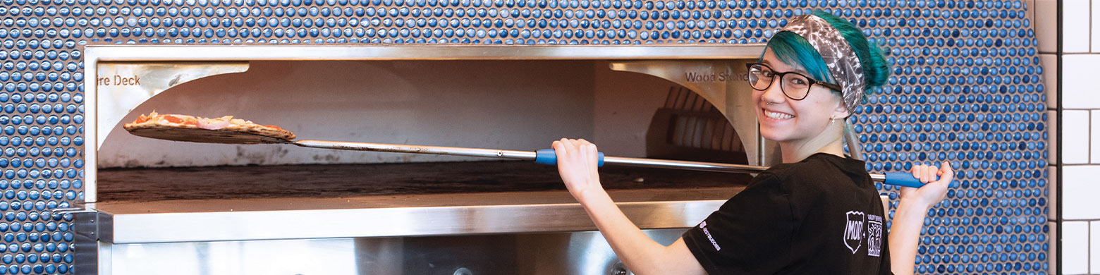 A MOD Squad member smiling while using the pizza oven.