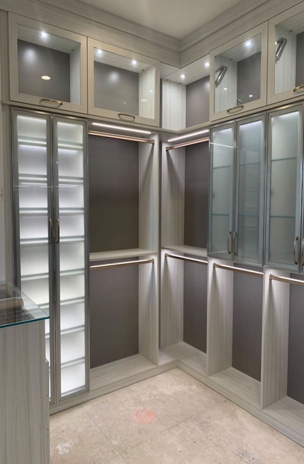 light grey wood custom closet with integrated lighting and aluminum framed doors