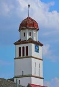 Außenansicht des Kirchturms in Grolsheim. Die prägenden Farben sind weiß und rot und die Grundform ist viereckig.
