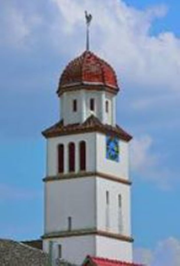 Außenansicht des Kirchturms in Grolsheim. Die prägenden Farben sind weiß und rot und die Grundform ist viereckig.