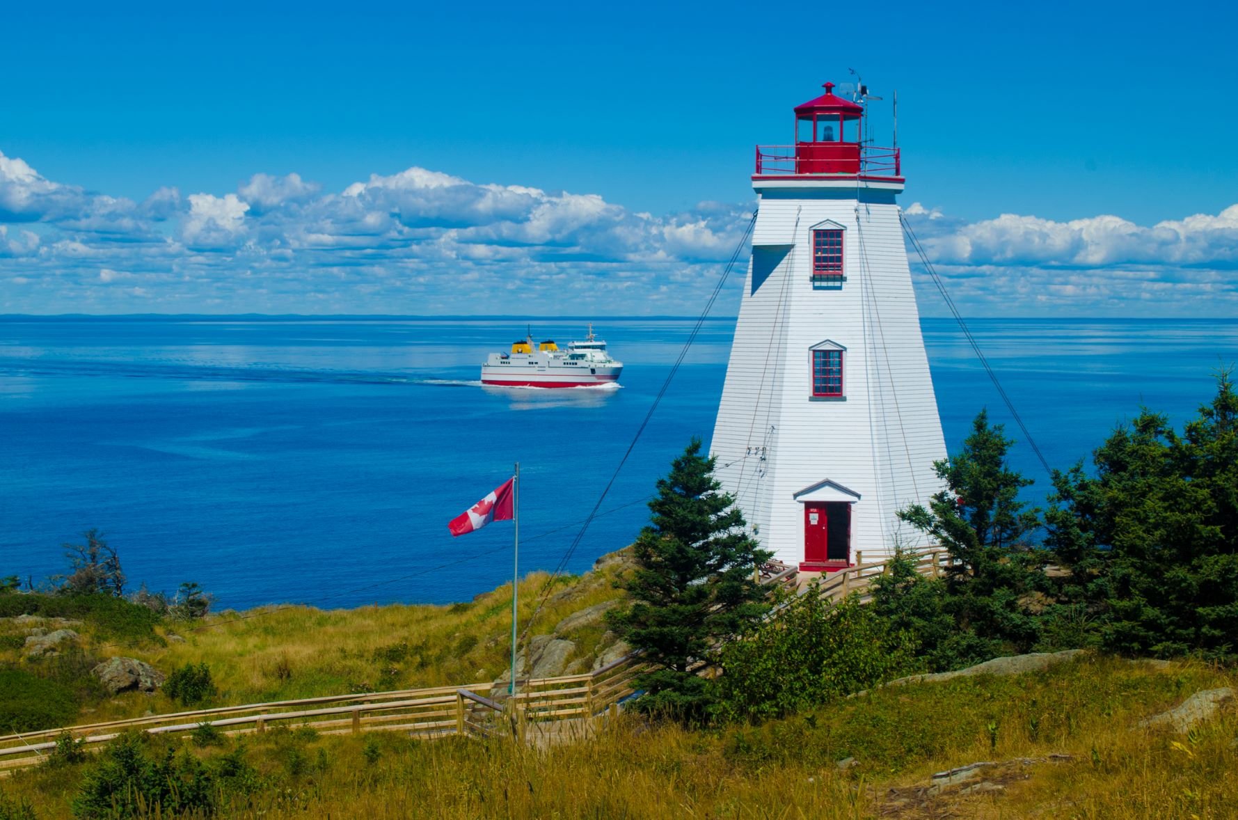 White and red lighthouse with a ferry going by across the ocean.