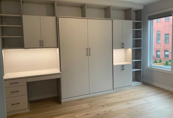 closed wall bed with cabinetry surrounding it with desk and integrated lighting