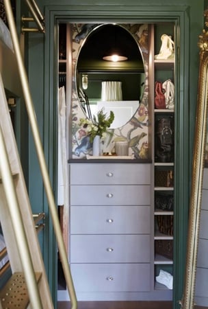 Green reach-in closet with flower wallpaper and floor-mounted white drawers.