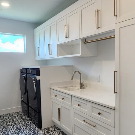Custom laundry room with white cabinetry, built-in storage, utility sink, countertop workspace, and stacked laundry appliances.