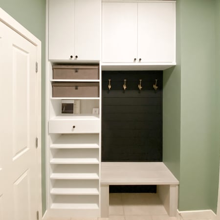 Small mudroom nook filled with upper cabinets, shoe shelves, a bench, and black shiplap with gold hooks.