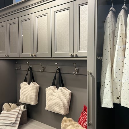 A custom entryway with coat hooks, a bench, shoe storage, overhead cabinet storage, and scarf rack located at California Closets Showroom in Woodmere, Ohio.