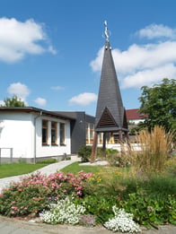 „Hell, klar, offen und einladend!“ – sollte der Raum sein. Lichtdurchbrüche über den Türen bringen Tageslicht in Flur und Foyer, die Türen zum Kirchenraum sind verglast, so dass die Besucherinnen und Besucher einen Blick auf Kirche und Altar haben. Und auf dem Glas der Kirchentüren deuten weiße Strahlen auf das Licht aus der Höhe.