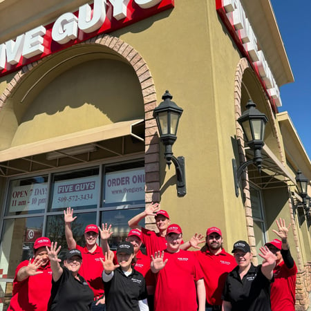 Exterior photograph of employees posing in front of the Five Guys restaurant at 2671 Queensgate Drive in Richland, Washington.