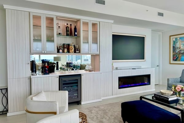 Custom entertainment center with built-in home bar, glass cabinetry, beverage refrigerator, television, and electric fireplace.