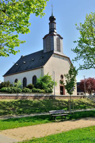 Das Kirchengebäude am Altrhein wurde 1746 nach den Plänen des Darmstädter Superintendenten Johann Konrad Lichtenberg anstelle einer Vorgängerkirche erbaut. 1944 legte ein Bombenangriff das Kirchengebäude bis auf die Grundmauern in Schutt und Asche. Unter großer Anteilnahme und mit Unterstützung der Ginsheimer Bevölkerung wurde dieses in schlichter Form wieder aufgebaut und 1953 durch den damaligen Kirchenpräsidenten Martin Niemöller eingeweiht. Das denkmalgeschützte Gotteshaus im Ensemble mit dem benachbarten Gemeindehaus liegt idyllisch direkt an den Spazier- und Radfahrwegen in der Auenlandschaft am Altrhein. Es prägt seit Jahrhunderten das Bild des Ortes. Die Kirche ist täglich für Besucherinnen und Besucher geöffnet.