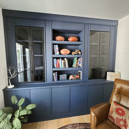 Deep blue bookcase with glass doors, open shelving, closed cabinetry, and lighting.