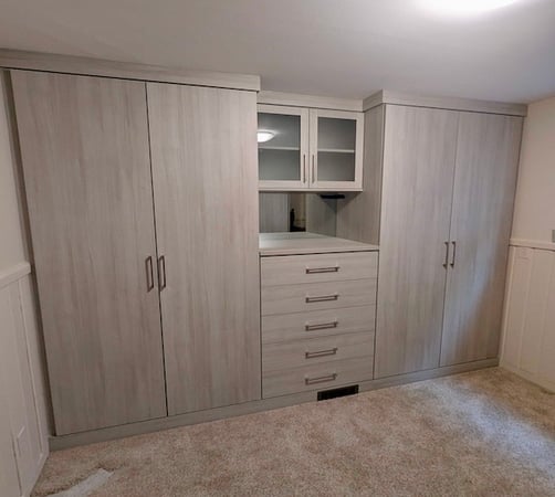 Custom wardrobe storage system featuring built-in cabinets, drawer organization, and frosted glass upper cabinetry for elevated bedroom organization. This custom closet solution by California Closets includes wardrobe cabinets, custom storage systems, and functional home organization designed to maximize bedroom storage space.