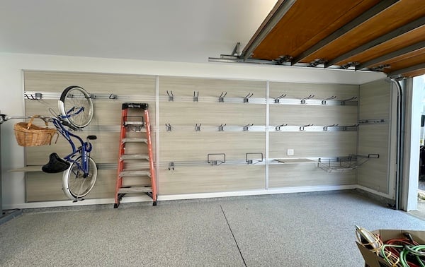 Custom garage storage with fusion track wall, bike hooks, baskets, shelves, and a ladder on a light wood-tone panel wall.