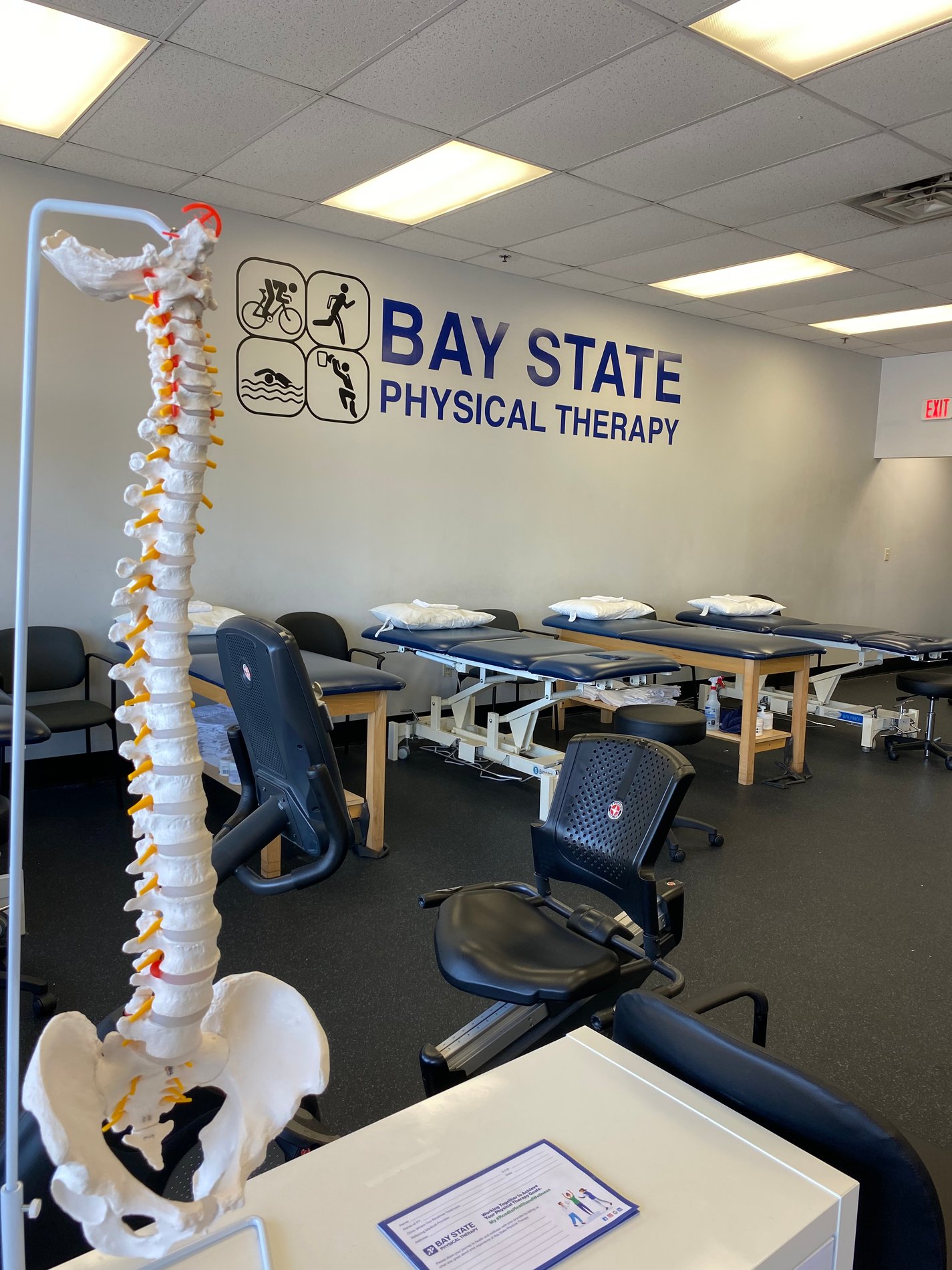 Inside Bay State Physical Therapy Chelmsford, MA Parkhurst St. showing spine and hip diagram, Bay State Logo on wall and PT patient tables in the background.