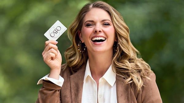 Woman is smiling and holding a Cato Fashions gift card.