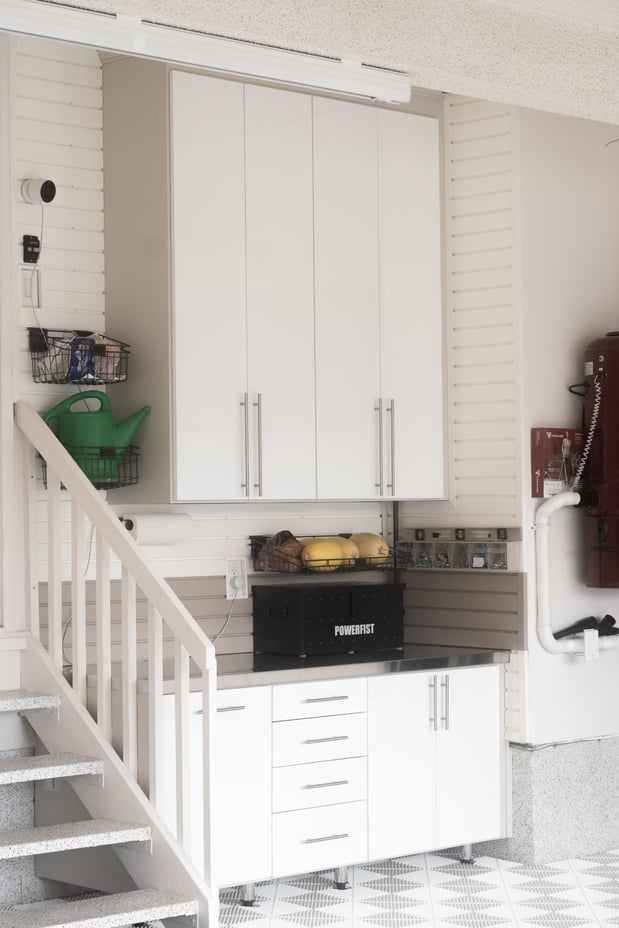 White garage with white floor tiles, gray slatwall, closed cabinets and drawers.