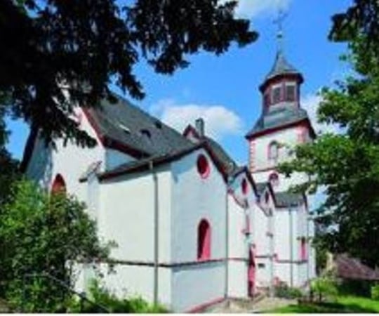 Außenansicht der weiß-roten Kirche mit schwarzem Dach umgeben von Grün.